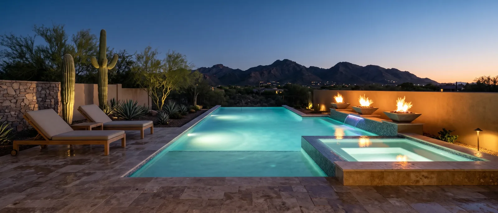 A new geometric pool and a raised, glass-tiled spa in a Scottsdale desert backyard at blue hour, the water lit turquoise, three fire bowls burning on a stucco wall, teak loungers, saguaro and mountains beyond.
